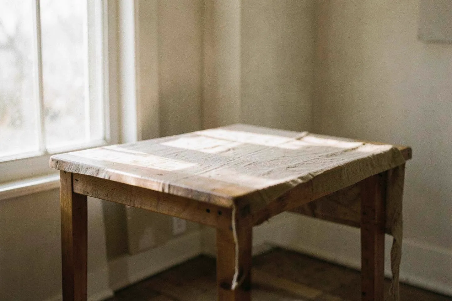 A plain wooden table beside a window in morning light